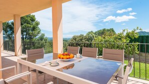 Un espace extérieur aménagé, abrité et doté d’une table pour deux, entouré de chaises, et offrant une vue sur un paysage luxuriant.