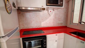 Una cocina compacta con horno empotrado, microondas y encimera roja.