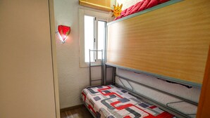 Una habitación pequeña y funcional con una cama litera, una ventana con vistas y una lámpara fijada a la pared.