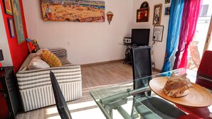 Un salón con sofá, una mesita de vidrio, televisor y diversas decoraciones en las paredes.
