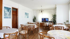 A dining area with multiple round tables and wicker chairs, a television in the background, and two paintings on the walls. - Mer Pansiyon (Fethiye)