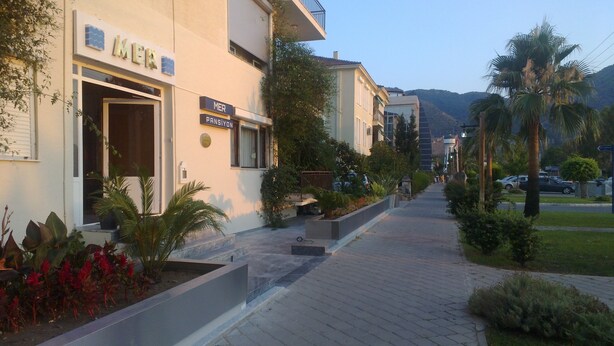 A hotel with a sign reading "MER PANSILYON" and a paved walkway with plants and palm trees. - Mer Pansiyon (Fethiye)