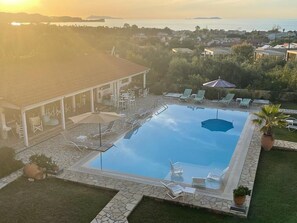 Une piscine extérieure dotée de chaises longues et de parasols, entourée d’une terrasse en pierre et offrant une vue sur la mer et la ville en arrière-plan.