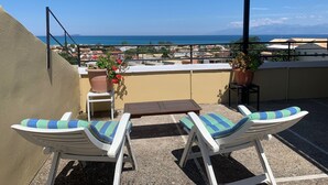 Una terraza en la azotea con dos sillones blancos, una mesita y plantas en macetas.