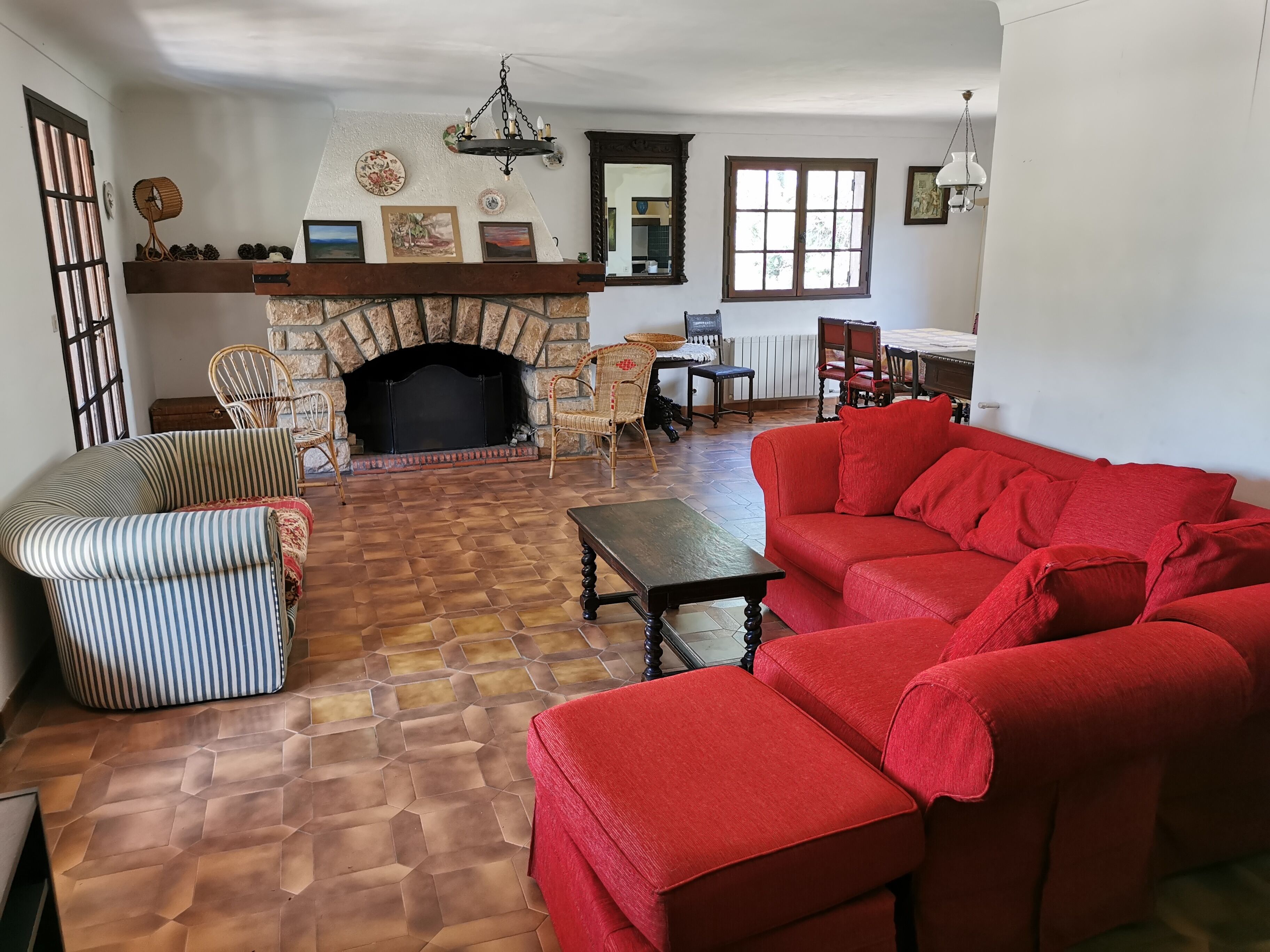 Un salon avec une cheminée en pierre, un canapé rouge, des fauteuils à rayures et une table basse en bois.