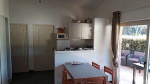 A compact kitchen with white cabinets, a microwave, and a small refrigerator. There is a dining table with chairs and a window with curtains.