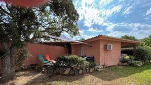 A small, single-story building with a red exterior, a covered patio area with outdoor seating, and a well-maintained garden.