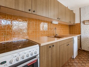 A kitchen with wooden cabinets, a stainless steel stove, a dishwasher, and patterned orange tiles.