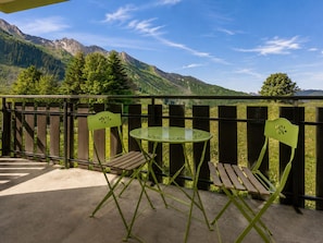 A balcony with a view of mountains, two green chairs, and a small round table.