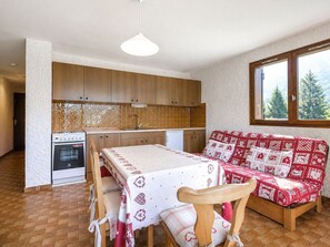 Kompakti keittiö, jossa on puukuvioiset kaapit, sisäänrakennettu uuni ja ruokapöytä punavalkoisella kuviollisella pöytäliinalla.