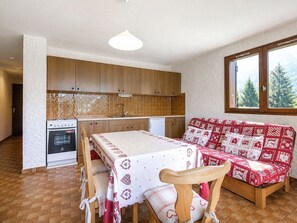 A compact kitchen with wooden cabinets, a built-in oven, and a dining table with a red and white patterned tablecloth.