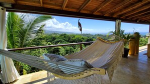 Un'amaca su un balcone con vista su vegetazione lussureggiante e montagne.