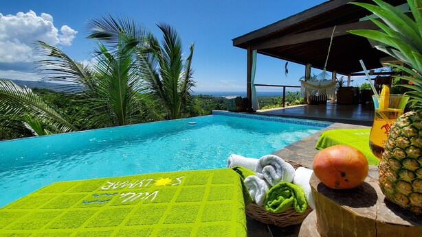 Zona piscina con vista sull'oceano, un'amaca e un'ananas.
