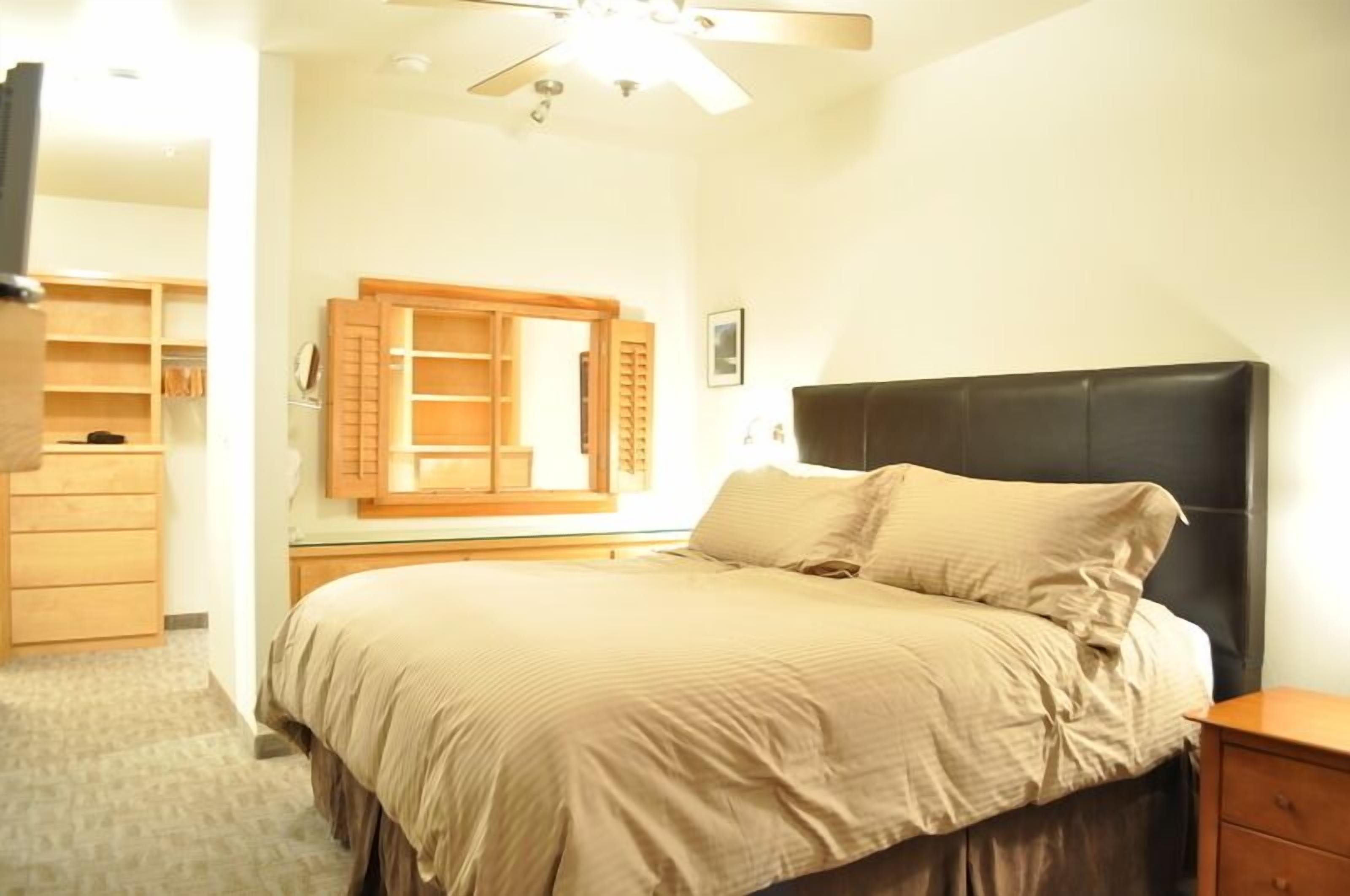 A bedroom with a bed, wooden wardrobe, and a ceiling fan.