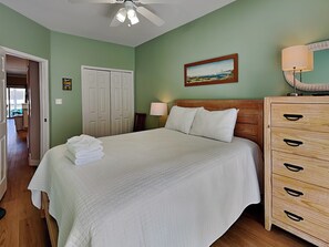 Un dormitorio con cama, cómoda de madera, un cuadro en la pared y ventilador de techo.