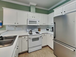Una cocina con armarios blancos, un refrigerador de acero inoxidable, un microondas y una estufa.