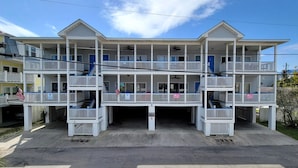 A multi-story hotel with balconies, a covered entrance, and a flag. - Tybee Sands 4A | Steps to Beach, Dining, Shops (Tybee Island)