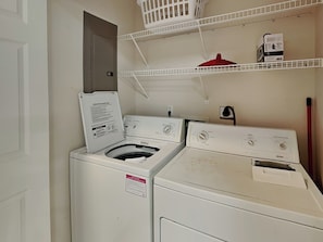 A laundry room with a front-loading washer and dryer, a white basket on a shelf, and a red pot on the dryer.