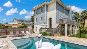 A swimming pool with a swan float, a house with a balcony, and a wooden deck. - Beach Digs | Bay View, Heated Pool, Steps to Beach (Tybee Island)