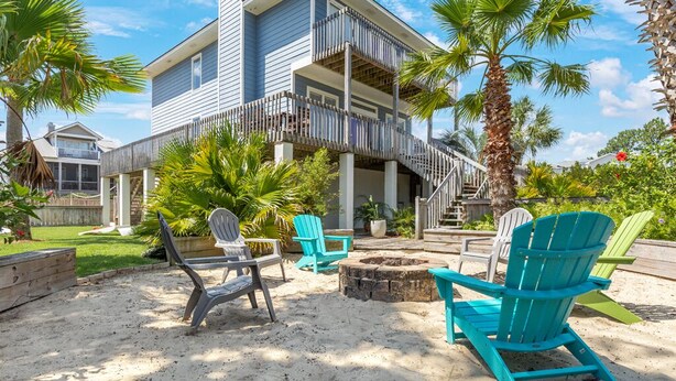 A beachfront property with a two-story building, outdoor seating area with chairs, and a fire pit. - Beach Digs | Bay View, Heated Pool, Steps to Beach (Tybee Island)