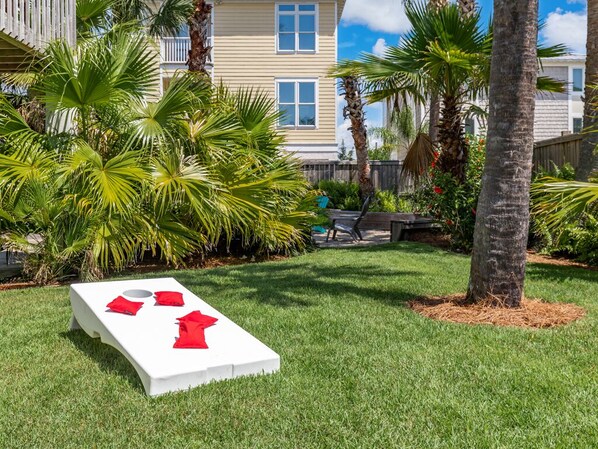 Un fauteuil de jardin blanc avec des coussins rouges, placé dans un espace verdoyant agrémenté de palmiers et avec un bâtiment en arrière-plan.