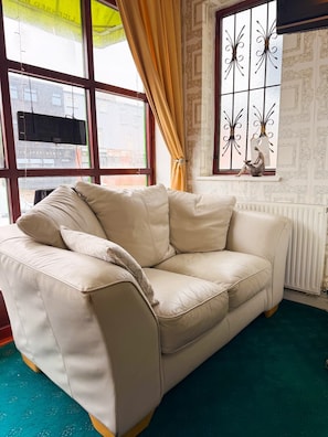 A beige leather sofa with cushions, positioned in front of a window with decorative iron grilles and curtains. - OYO Wynnstay Hotel (Blackpool)