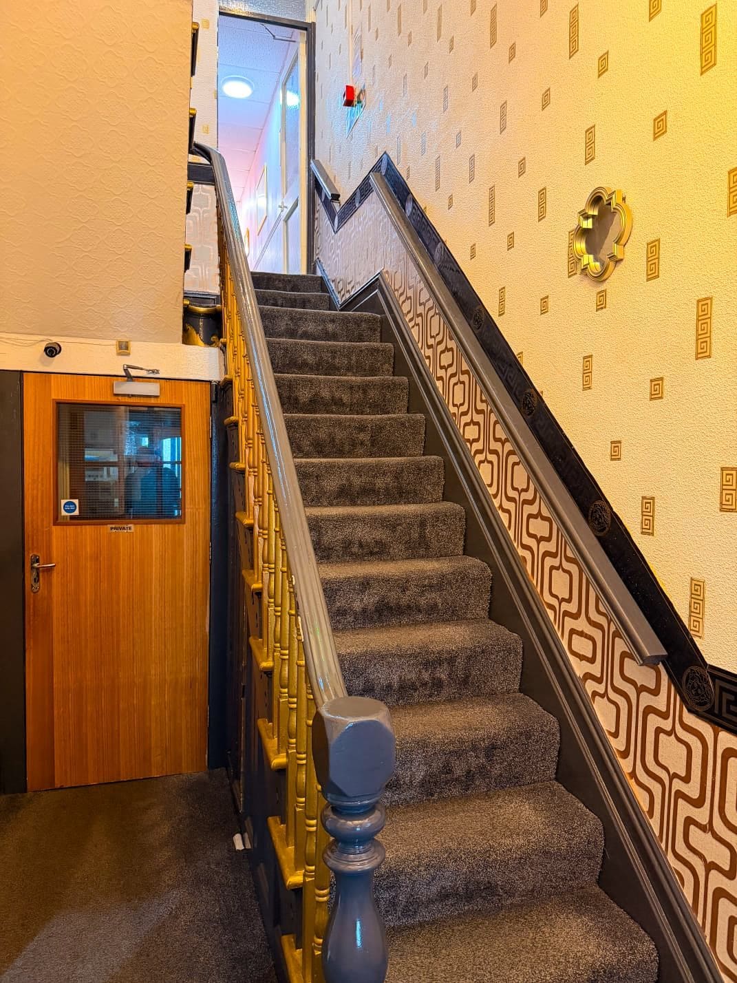 A carpeted staircase with a patterned wall and a wooden door labeled 'PRIVATE.'