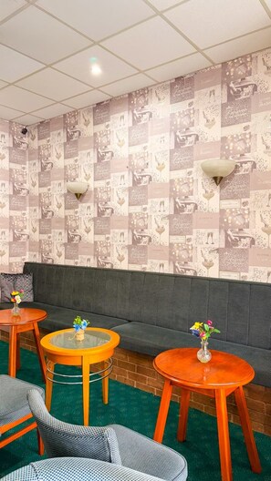 A room with a patterned wallpaper, a sofa, two round tables with vases, and a green carpet. - OYO Wynnstay Hotel (Blackpool)