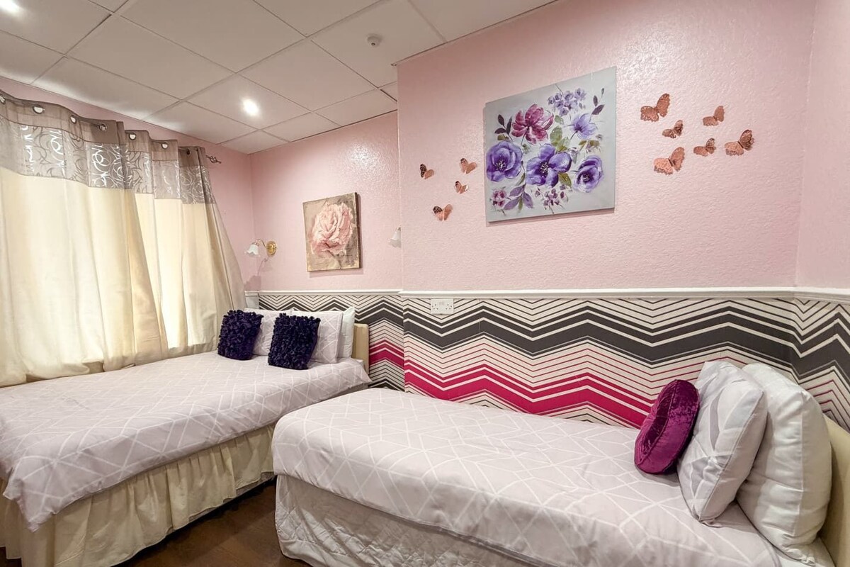 A bedroom with two beds, a decorative wall with butterfly stickers, and a floral painting.