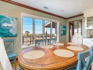 Enjoy meals in this dining area with a round table and six chairs, surrounded by large windows offering a view of the outdoors and a wooden deck.