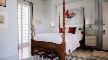 A four-poster bed with a wooden frame and white bedding, a nightstand with a lamp, and a painting above the bed.