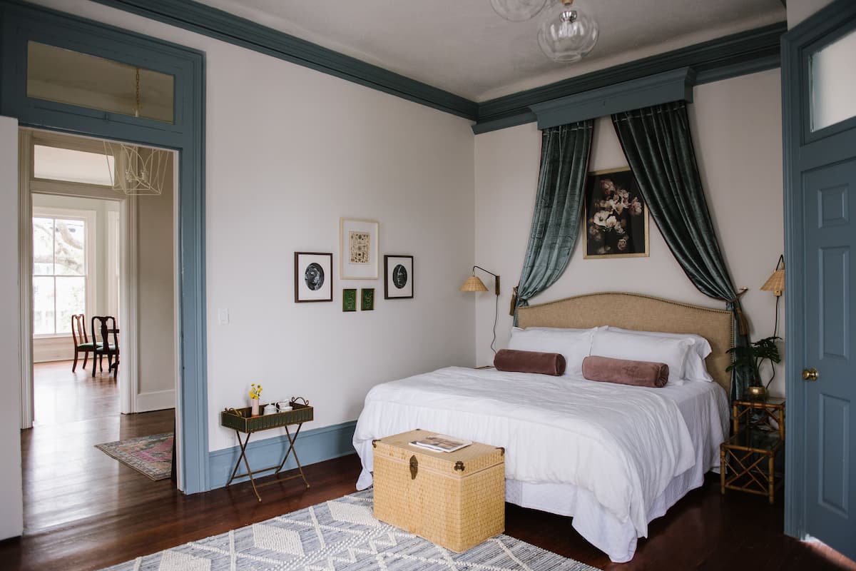 A bedroom with a large bed, a bedside table, a lamp, and a window with curtains.