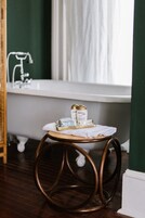 Une salle de bain avec une baignoire blanche, un tabouret en bois sur lequel sont posées des bouteilles, et un miroir.