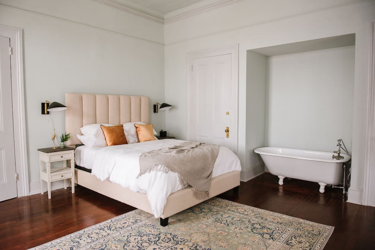 A bedroom with a bed, bedside tables, a nightstand, a large rug, and a white door.