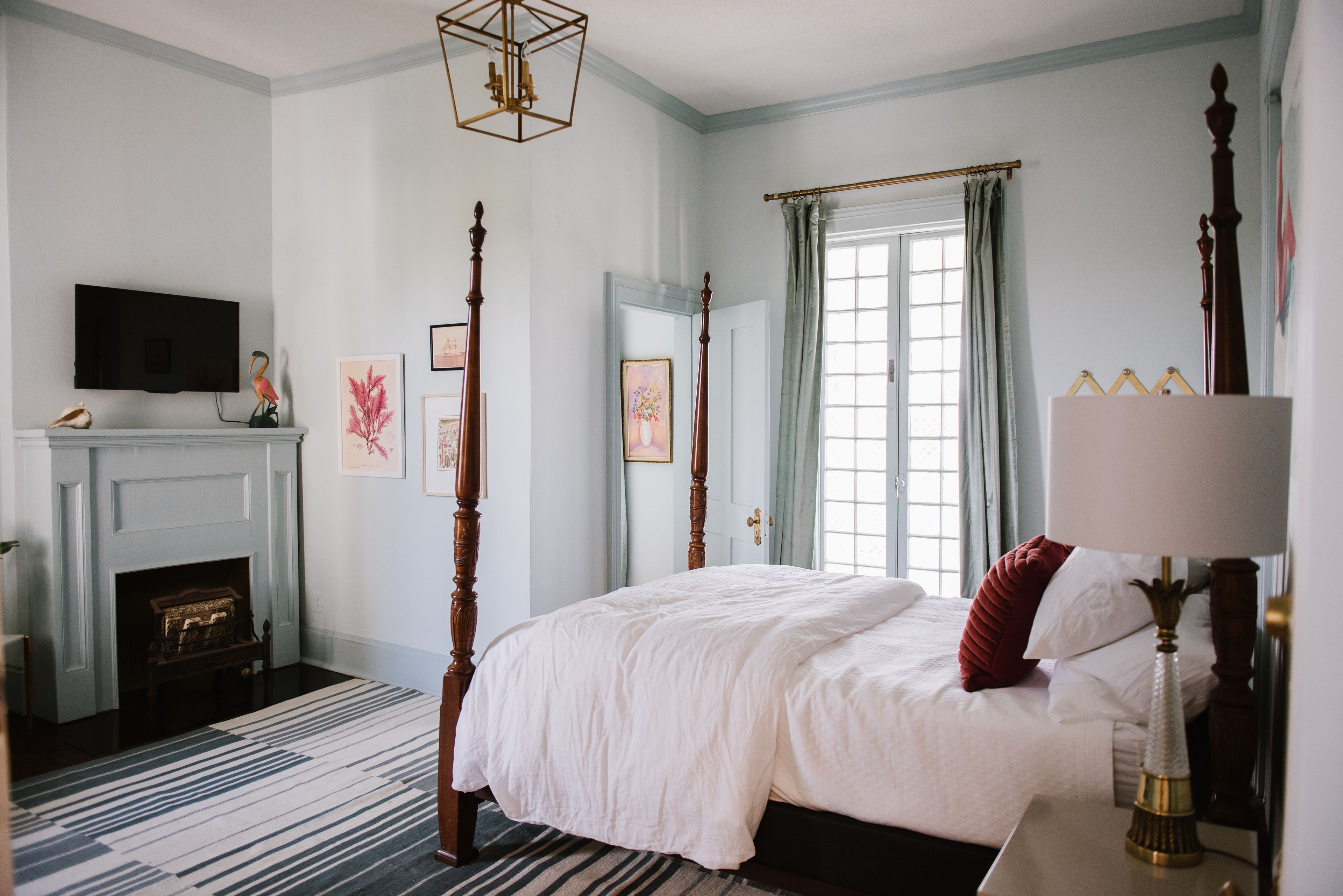 A bedroom with a four-poster bed, a fireplace, a television, and a window with curtains.
