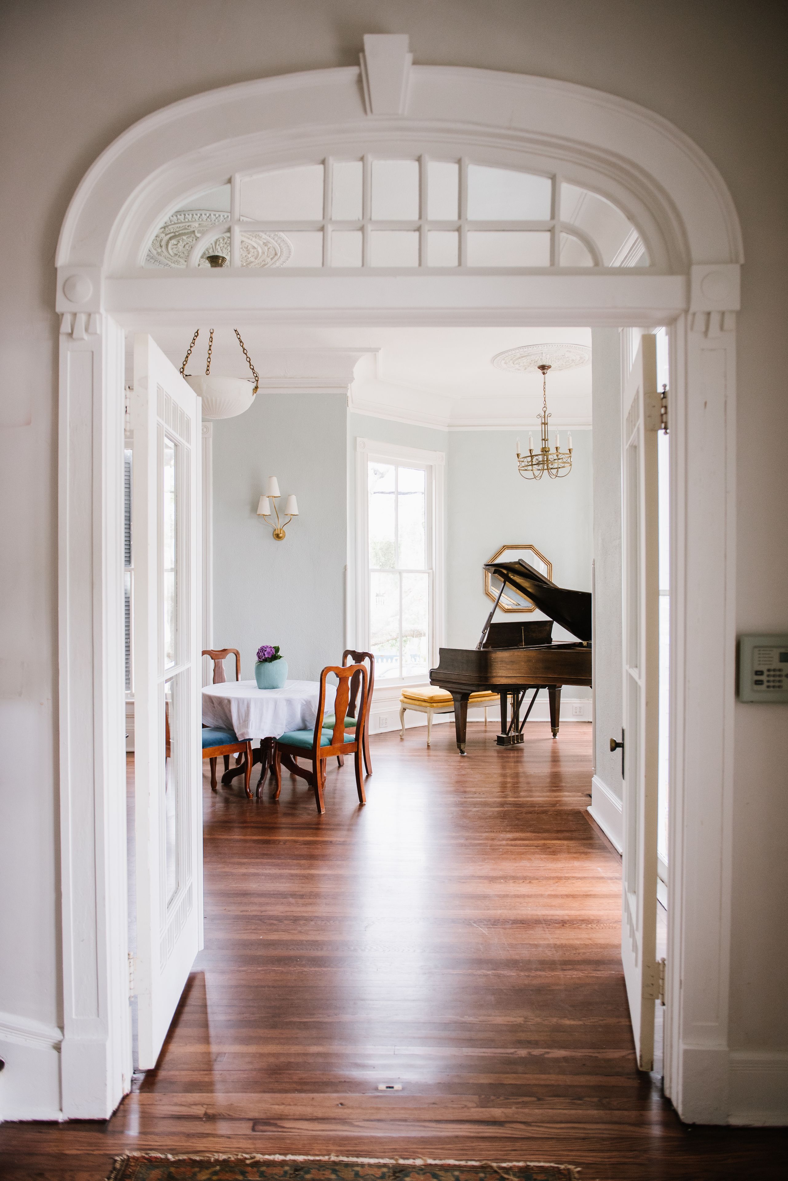 A grand room with a piano, a dining table with chairs, and a chandelier.