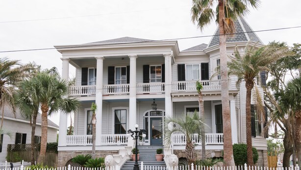A two-story house with a front porch, a staircase, and a white picket fence. - Carr Mansion (Galveston)