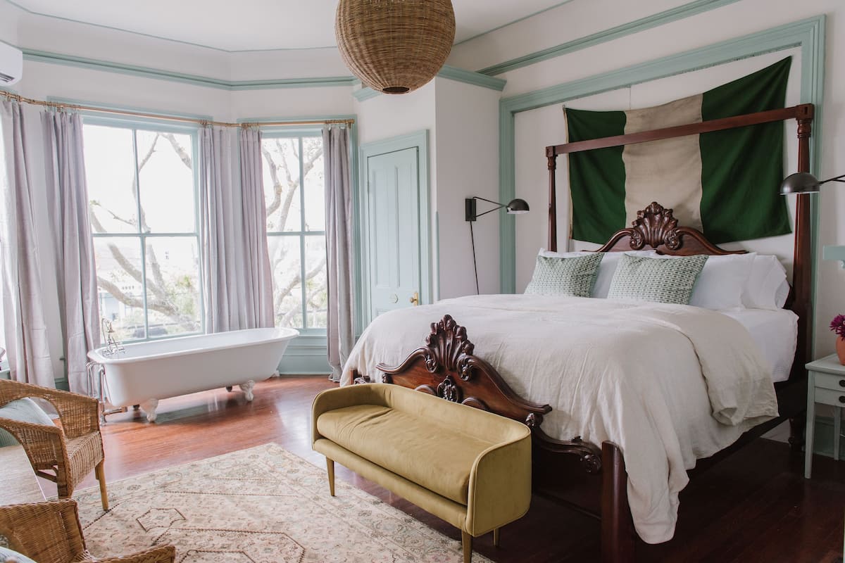 A bedroom with a large bed, a vintage bathtub, and a wicker bench.