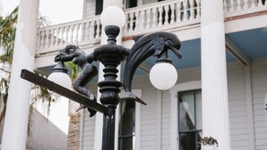 A street lamp with decorative elements and a building with balconies in the background. - Carr Mansion (Galveston)