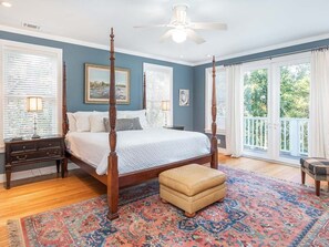 A bedroom with a four-poster bed, a large window with blinds, a ceiling fan, and a view of the outdoors. - Surf Shack | Luxurious Home, Plenty of Room! (Tybee Island)