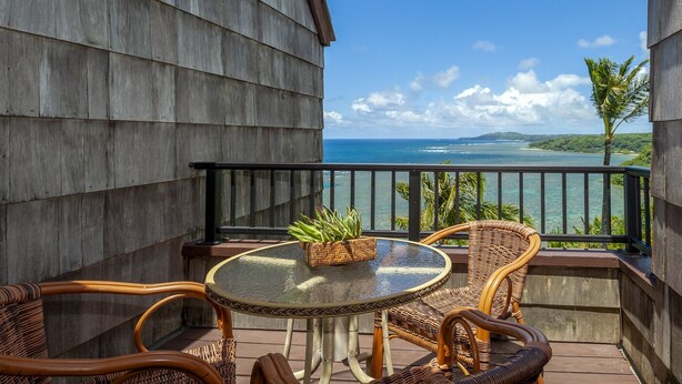 A balcony with wicker furniture, a glass table, and a potted plant. - Oceanfront and updated, top floor, perfect for honeymoon (Princeville)