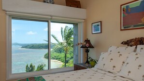 A bedroom with a large window offering a view of the ocean and palm trees. - Oceanfront and updated, top floor, perfect for honeymoon (Princeville)