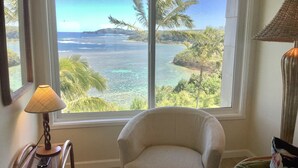 A room with a large window offering a view of a tropical beach and ocean. - Oceanfront and updated, top floor, perfect for honeymoon (Princeville)