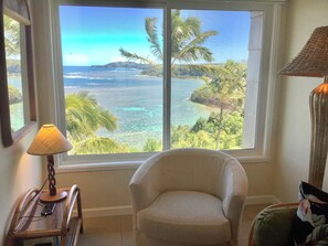 A room with a large window offering a view of a tropical beach and ocean. - Oceanfront and updated, top floor, perfect for honeymoon (Princeville)