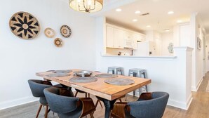 A dining area with a wooden table and grey upholstered chairs, a woven pendant light, and decorative wall art. - Beach House 413 | Oceanfront, Pet Friendly, Pools (Tybee Island)