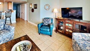 A living room with a TV, a blue armchair, and a patterned sofa. - Beach House 442 | Oceanfront, Pet Friendly, Pools (Tybee Island)