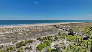 A beach with a wooden boardwalk leading to the shore, sandy beach, and sparse vegetation. - Beach House 442 | Oceanfront, Pet Friendly, Pools (Tybee Island)
