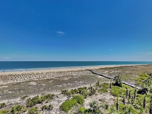 A beach with a wooden boardwalk leading to the shore, sandy beach, and sparse vegetation.