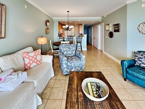 A living room with a sofa, armchair, coffee table, and a dining area with chairs and a table.