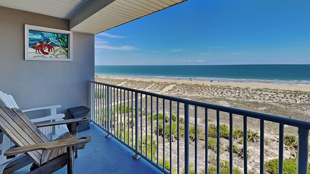 A balcony with a view of the beach, a framed painting, and outdoor furniture. - Beach House 442 | Oceanfront, Pet Friendly, Pools (Tybee Island)